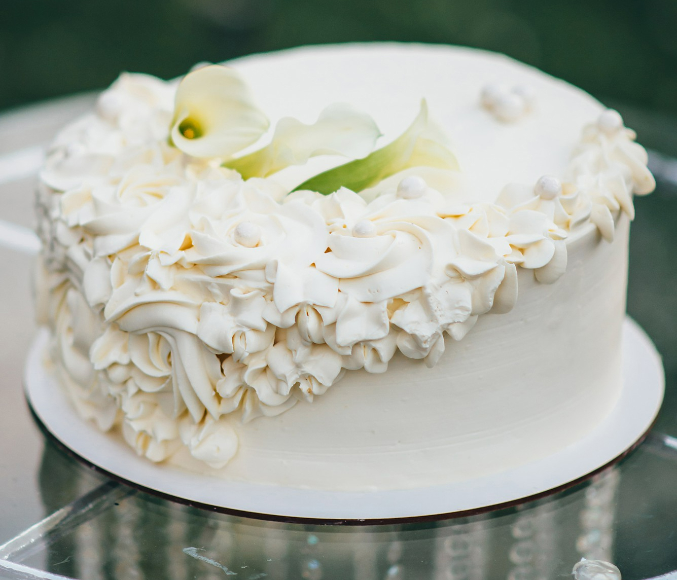 single-tiered-white-wedding-cake-decorated-with-cream-form-flowers-stands-glass-table-nature