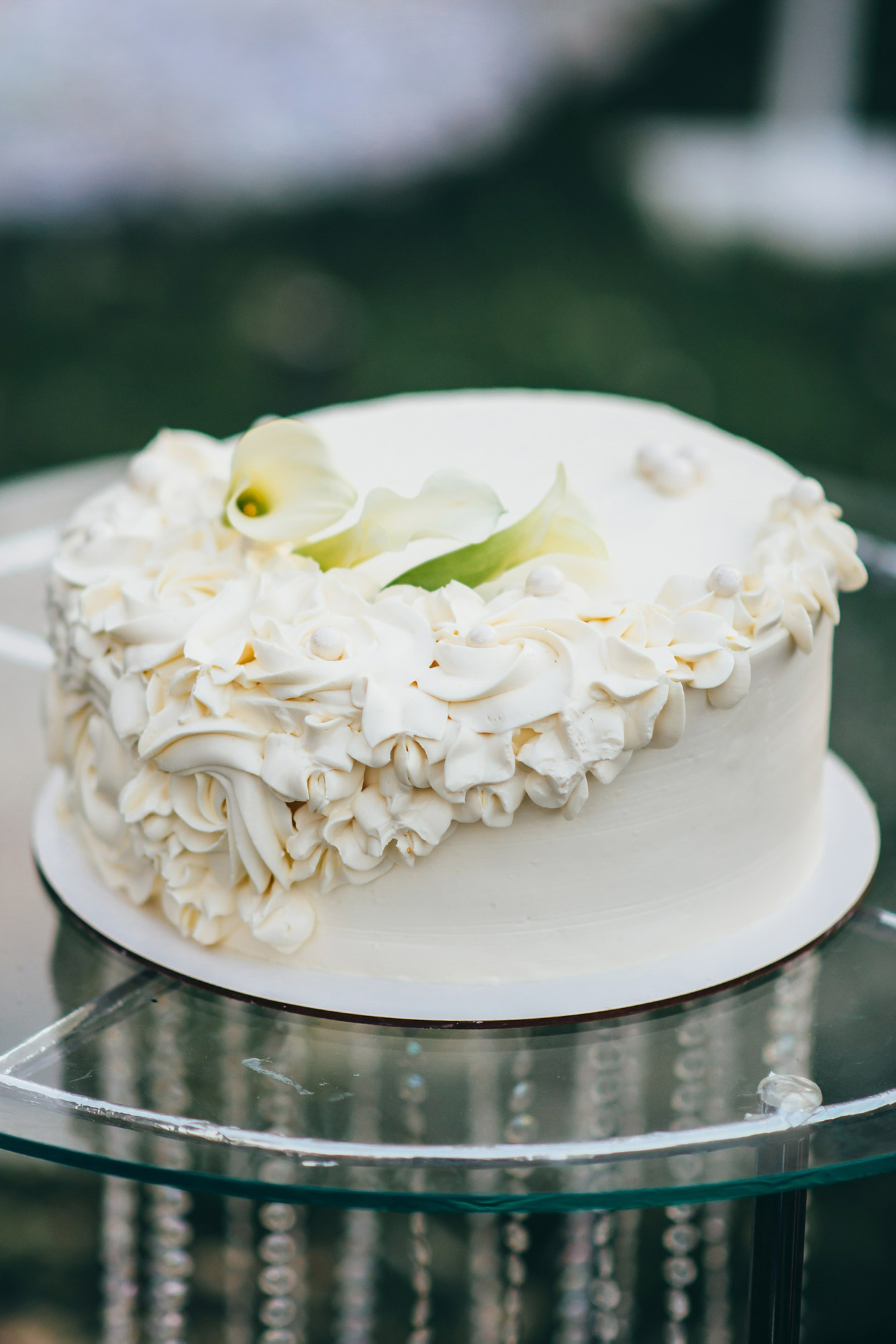 single-tiered-white-wedding-cake-decorated-with-cream-form-flowers-stands-glass-table-nature